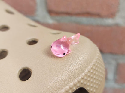 Close-up of glow-in-the-dark shark charms on a shoe shoe, showcasing their detailed design and soft, glowing effect. The sharks are securely attached, and their luminous feature adds a fun, ocean-inspired touch to the shoe in a dark setting.