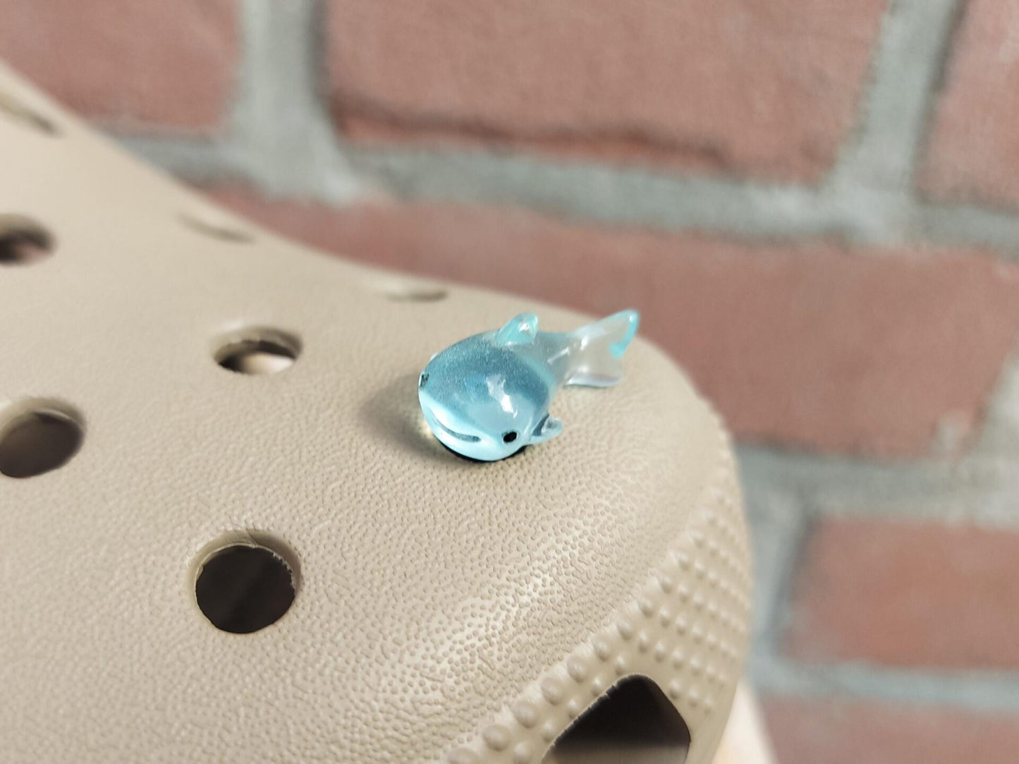 Close-up of glow-in-the-dark shark charms on a shoe shoe, showcasing their detailed design and soft, glowing effect. The sharks are securely attached, and their luminous feature adds a fun, ocean-inspired touch to the shoe in a dark setting.