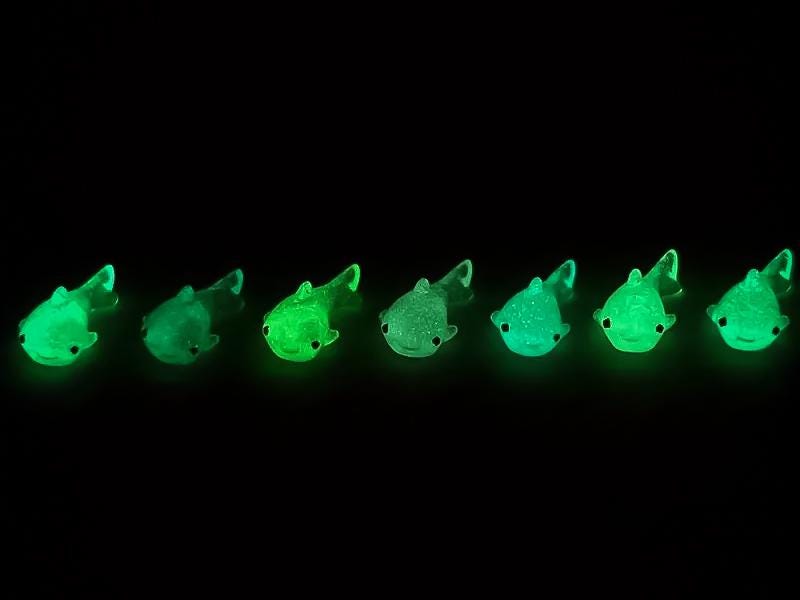 Close-up of glow-in-the-dark shark charms on a shoe shoe, showcasing their detailed design and soft, glowing effect. The sharks are securely attached, and their luminous feature adds a fun, ocean-inspired touch to the shoe in a dark setting.