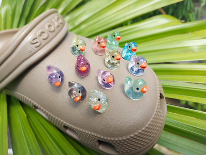 Close-up of glitter duck charms on a clog shoe, featuring sparkling, glitter-coated duck designs. The charms are securely attached, adding a fun and eye-catching shimmer to the shoe with a playful, vibrant look."