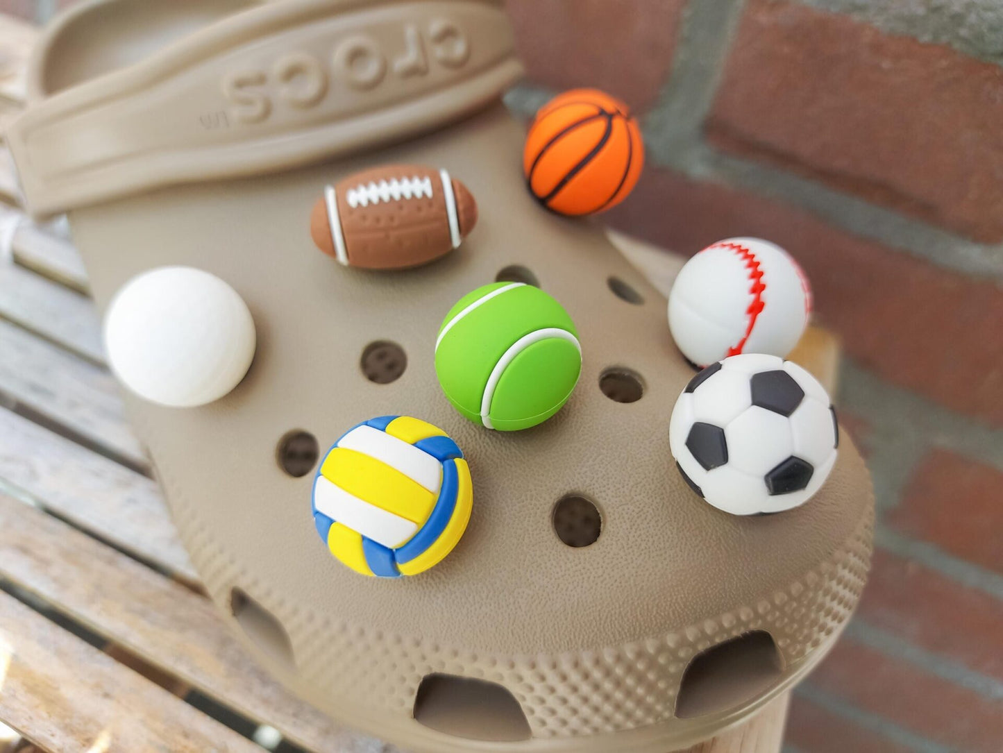 Close-up of a set of 7 sports-themed charms on a shoe shoe, featuring a basketball, football, soccer ball, tennis ball, baseball, volleyball, and golf ball. The charms are securely attached, adding a fun, athletic touch to the shoe.