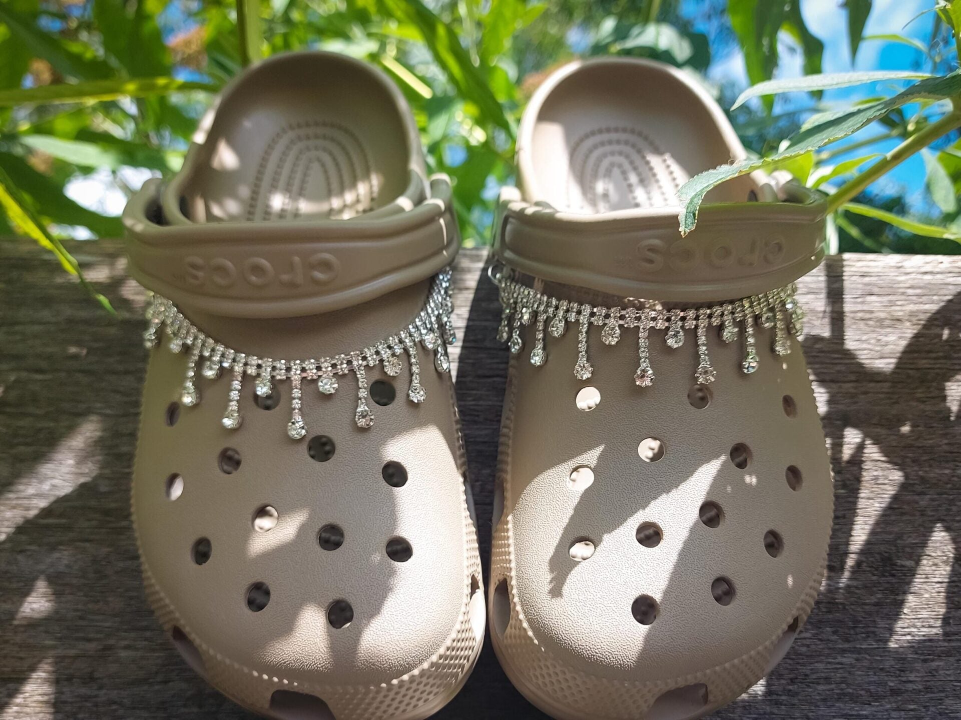 Close-up of a rhinestone chain charm draped across a pair of shoes, featuring sparkling rhinestones that catch the light. The chain is securely attached, adding a chic and luxurious touch to the shoes with its elegant, shimmering design.