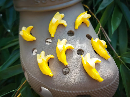 Close-up of a set of bright yellow banana charms on a pair of shoes, arranged playfully across the shoe. The banana charms add a quirky and cheerful touch, creating a fun and tropical look.