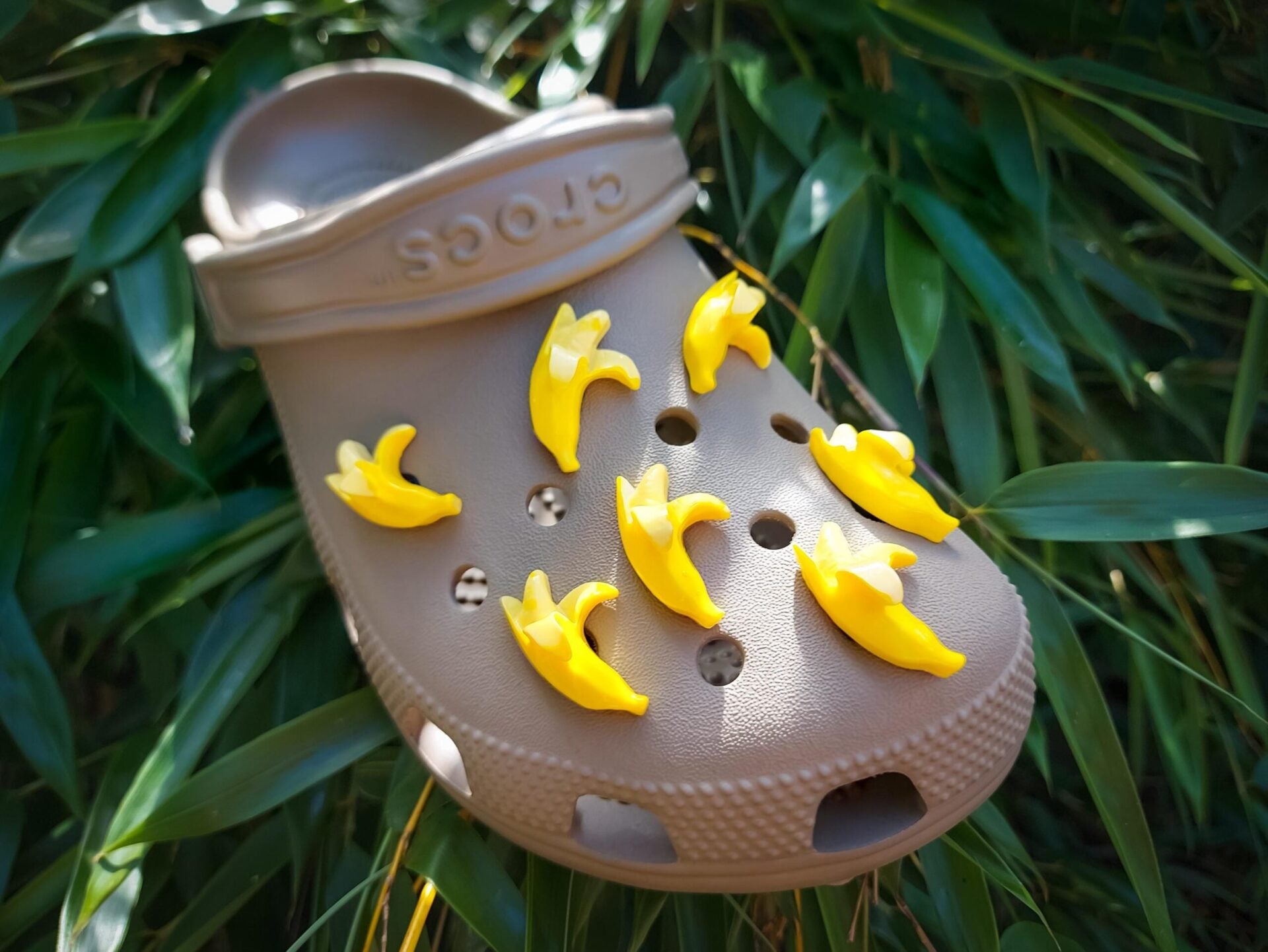 Close-up of a set of bright yellow banana charms on a pair of shoes, arranged playfully across the shoe. The banana charms add a quirky and cheerful touch, creating a fun and tropical look.