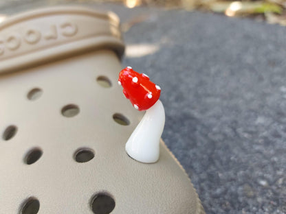 Glow in the dark forest mushroom shoe charms with white stems and red caps with white dots on a pair of shoes shoes.