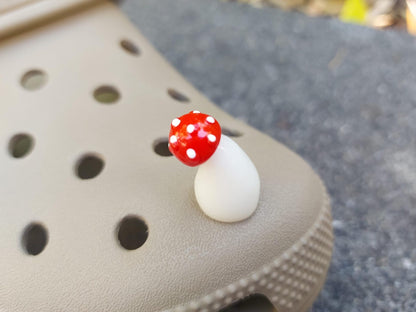 Glow in the dark forest mushroom shoe charms with white stems and red caps with white dots on a pair of shoes shoes.