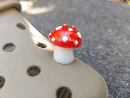 Glow in the dark forest mushroom shoe charms with white stems and red caps with white dots on a pair of shoes shoes.