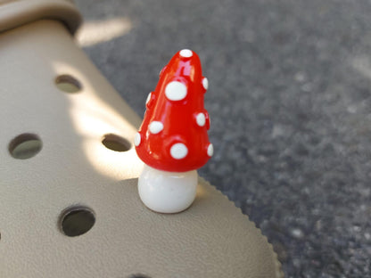 Glow in the dark forest mushroom shoe charms with white stems and red caps with white dots on a pair of shoes shoes.