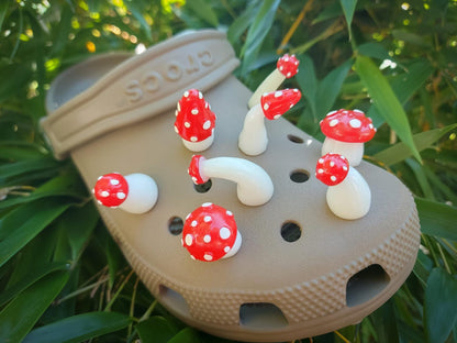 Glow in the dark forest mushroom shoe charms with white stems and red caps with white dots on a pair of shoes shoes.
