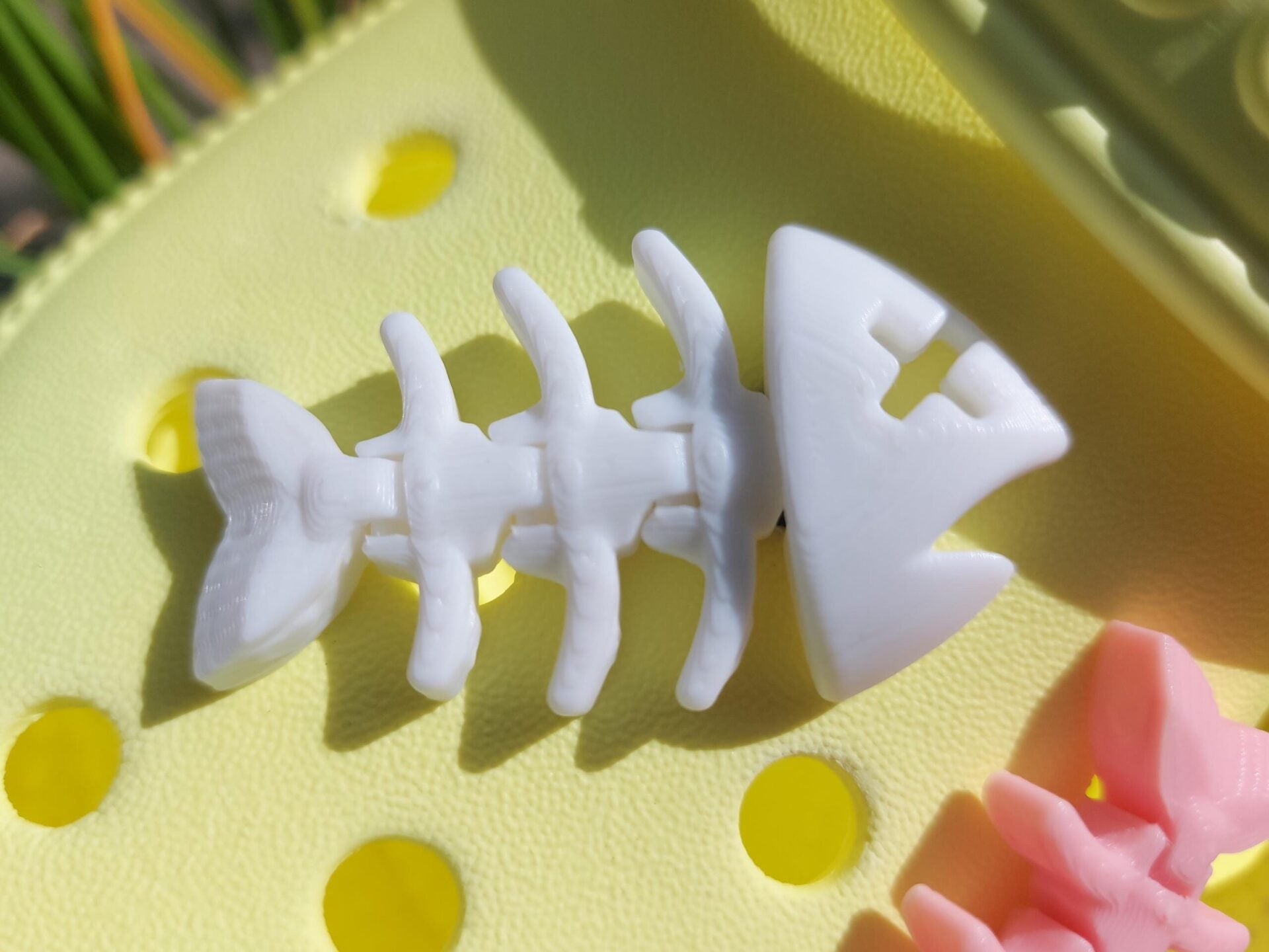 Yellow shoes adorned with colorful 3D-printed articulated fish bone charms in white, pink, black, teal, and yellow, displayed on a grassy background.