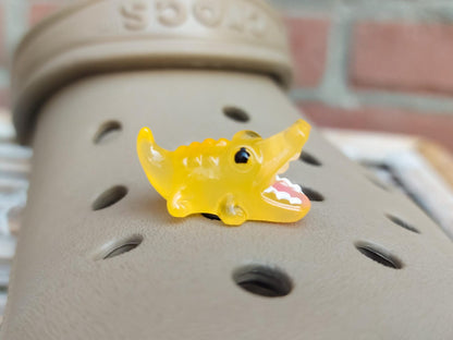 A set of glow-in-the-dark shoeodile charms adorns a shoes shoe. Each charm is shaped like a small, detailed shoeodile, appearing in a range of bright colors that glow vividly in the dark.