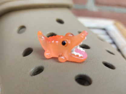 A set of glow-in-the-dark shoeodile charms adorns a shoes shoe. Each charm is shaped like a small, detailed shoeodile, appearing in a range of bright colors that glow vividly in the dark.