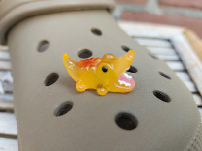 A set of glow-in-the-dark shoeodile charms adorns a shoes shoe. Each charm is shaped like a small, detailed shoeodile, appearing in a range of bright colors that glow vividly in the dark.