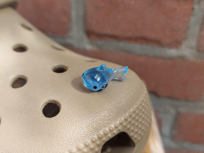 Close-up of glow-in-the-dark shark charms on a shoe shoe, showcasing their detailed design and soft, glowing effect. The sharks are securely attached, and their luminous feature adds a fun, ocean-inspired touch to the shoe in a dark setting.