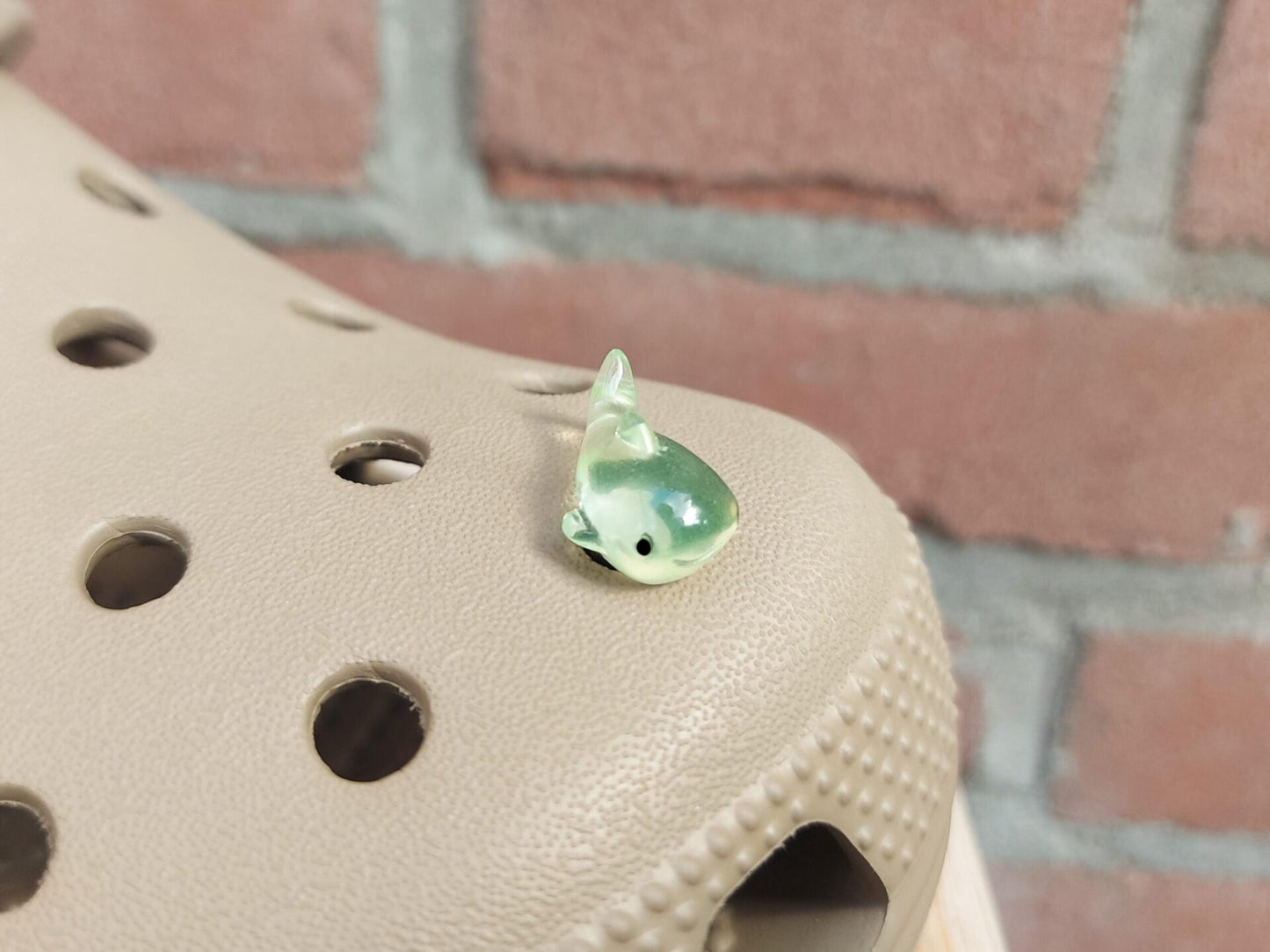 Close-up of glow-in-the-dark shark charms on a shoe shoe, showcasing their detailed design and soft, glowing effect. The sharks are securely attached, and their luminous feature adds a fun, ocean-inspired touch to the shoe in a dark setting.