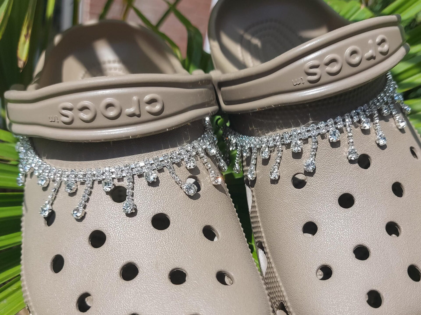 Close-up of a rhinestone chain charm draped across a pair of shoes, featuring sparkling rhinestones that catch the light. The chain is securely attached, adding a chic and luxurious touch to the shoes with its elegant, shimmering design.