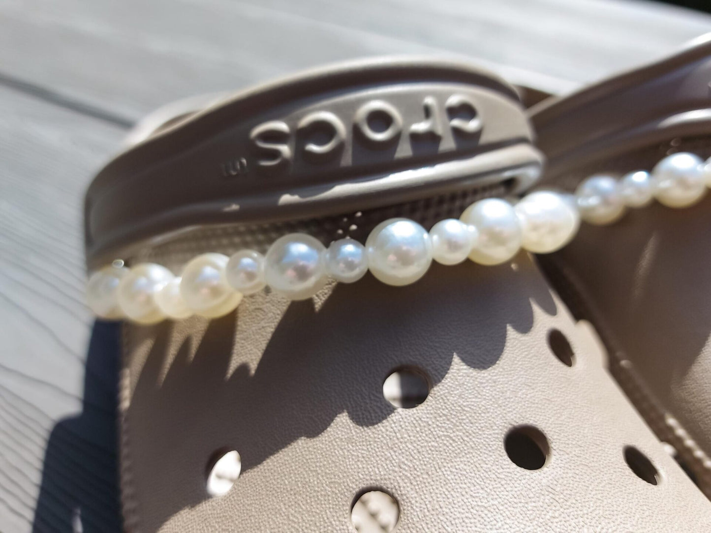Close-up of a white pearl chain charm on a pair of shoes, featuring a string of lustrous pearls elegantly draped across the shoe. The charm adds a classic and timeless touch to the footwear, creating a sophisticated and luxurious look.