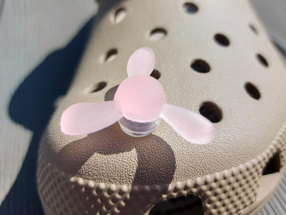 Close-up of glow-in-the-dark windmill shoe charms attached to a beige shoe, displayed outdoors in sunlight. The colorful windmill blades spin as you walk, adding a fun, dynamic feature to your shoes.