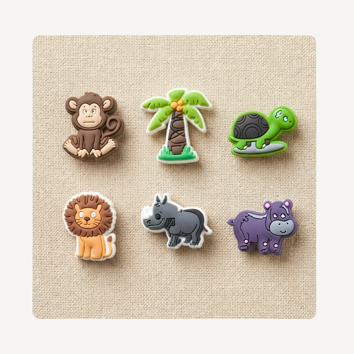 Six cartoon animal and nature-shaped clog charms arranged on a beige textured square background. The designs include a brown monkey, a green palm tree, a green turtle, a tan lion, a gray rhinoceros, and a purple hippo, each with simple facial features.