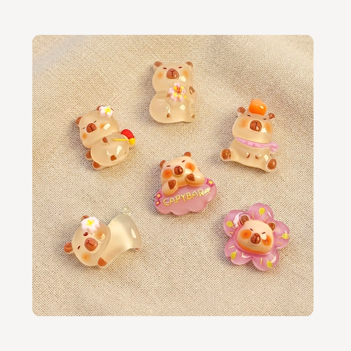 Six small decorative animal-shaped clog charms arranged on a beige fabric background. The characters are cream and peach with pastel accents including pink, yellow, orange, and purple.