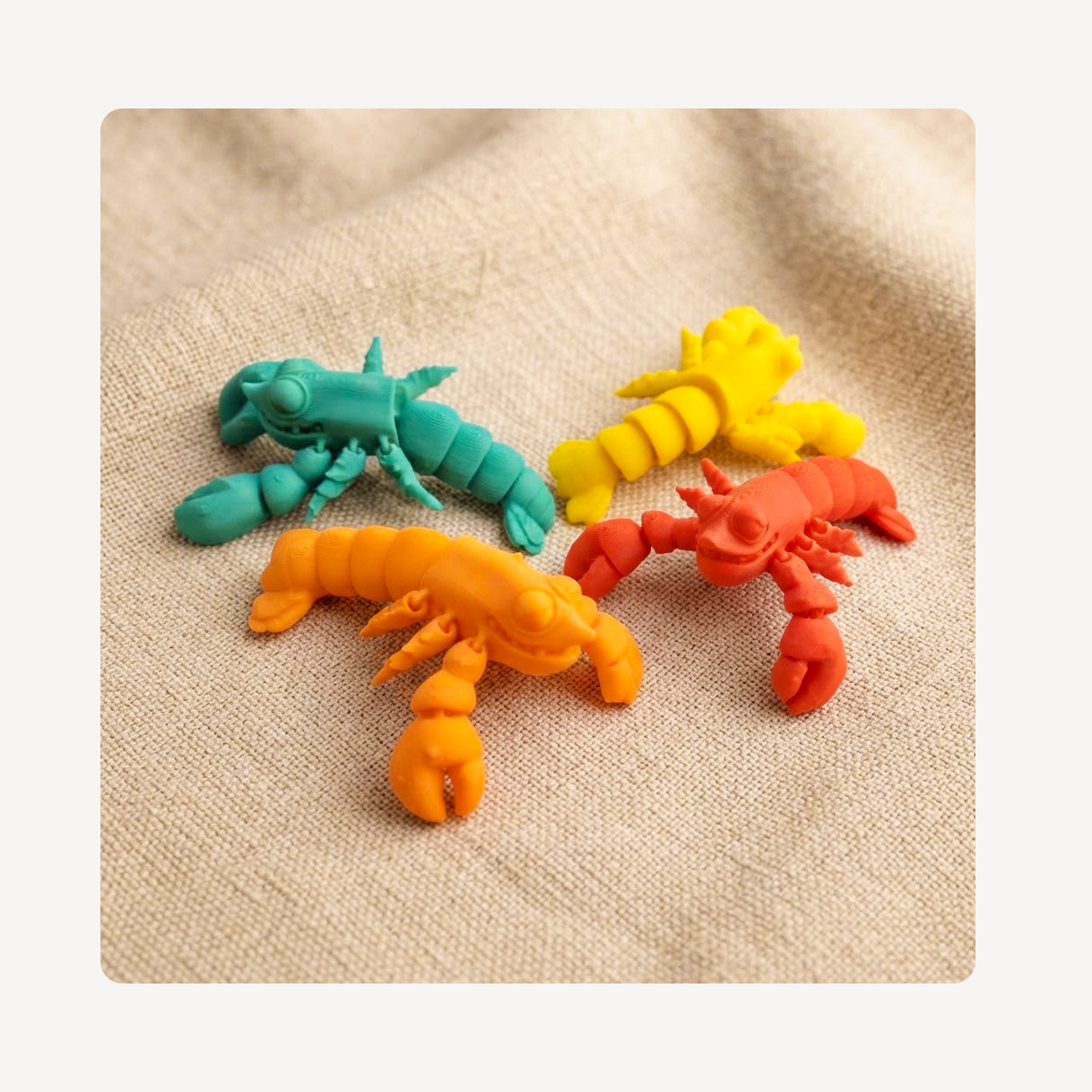 Four small lobster-shaped clog charms in teal, yellow, orange, and red, arranged on a beige textured fabric background.