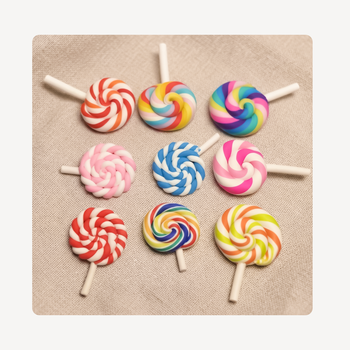 Nine colorful spiral lollipop clog charms arranged in a 3x3 grid on a beige textured fabric background.