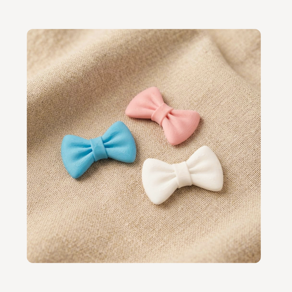 Three small bow tie-shaped clog charms in a textured plastic material, centered on a beige woven surface.