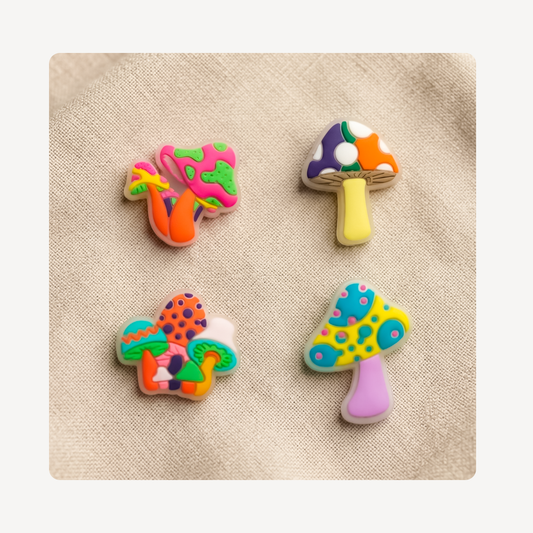 Four colorful mushroom-shaped clog charms arranged on a beige textured fabric background.