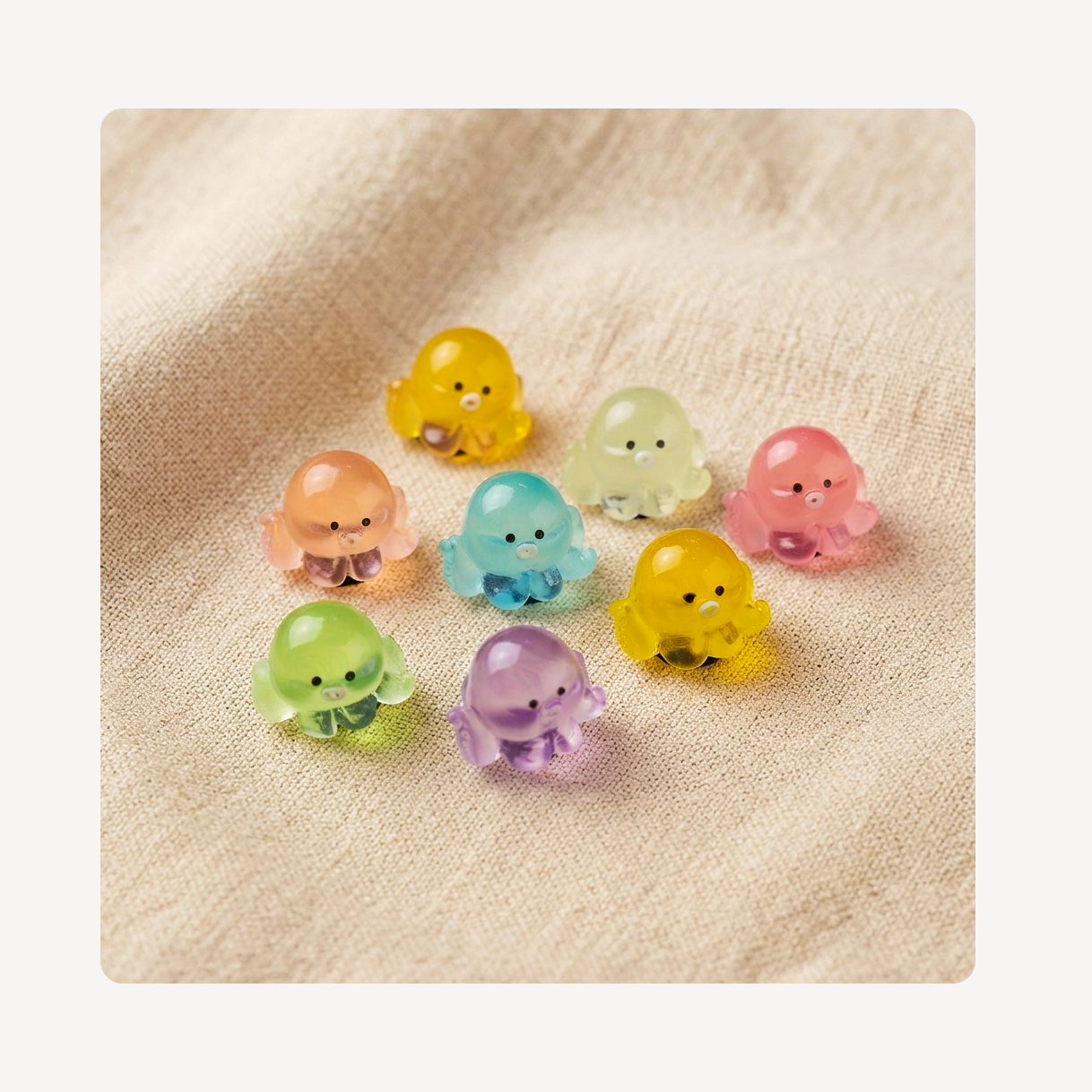 Eight small translucent octopus-shaped clog charms in assorted pastel colors, including yellow, pink, blue, green, and purple, arranged on a beige textured fabric background.