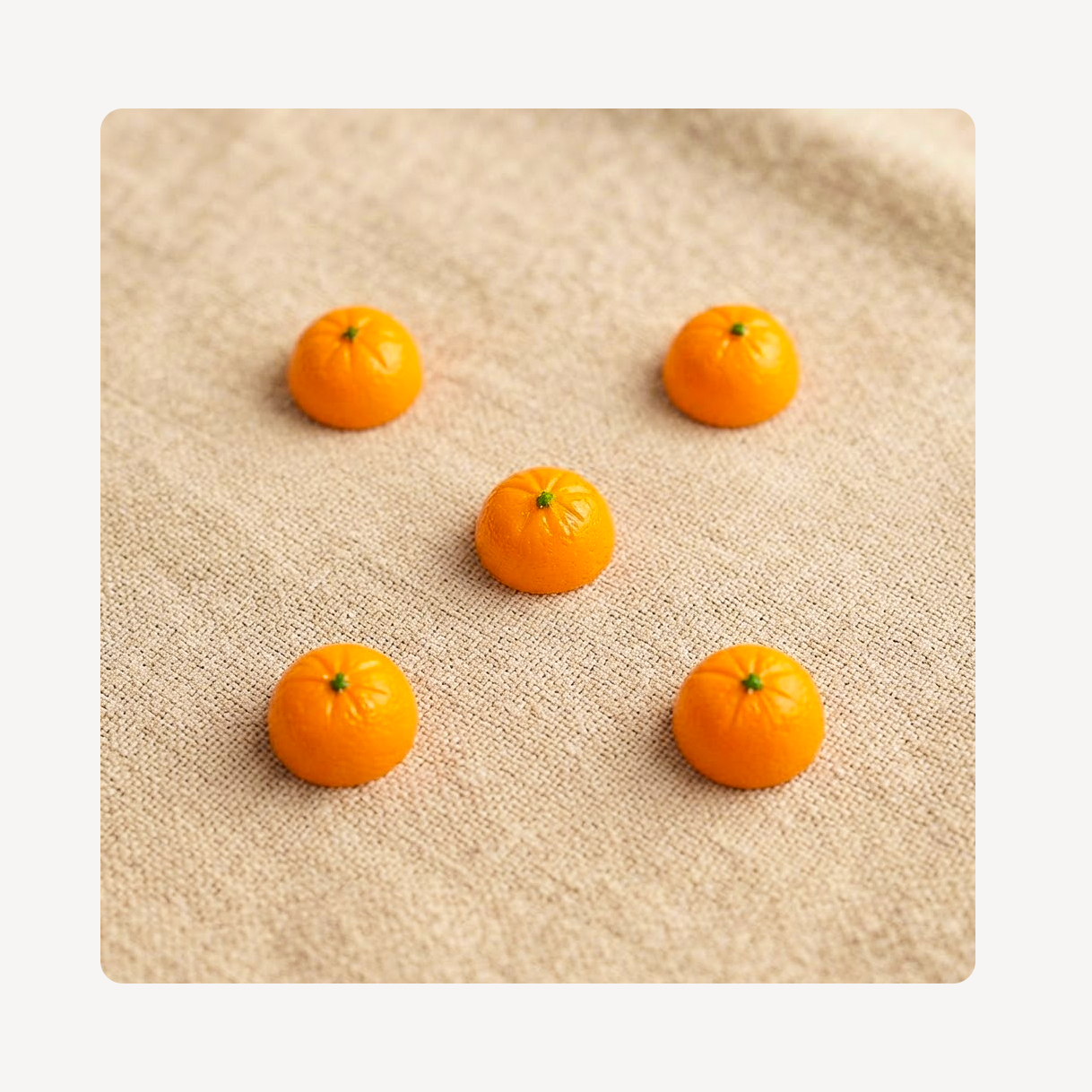 Five small orange clog charms arranged on a beige textured fabric background.