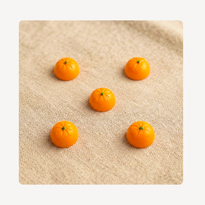 Five small orange clog charms arranged on a beige textured fabric background.