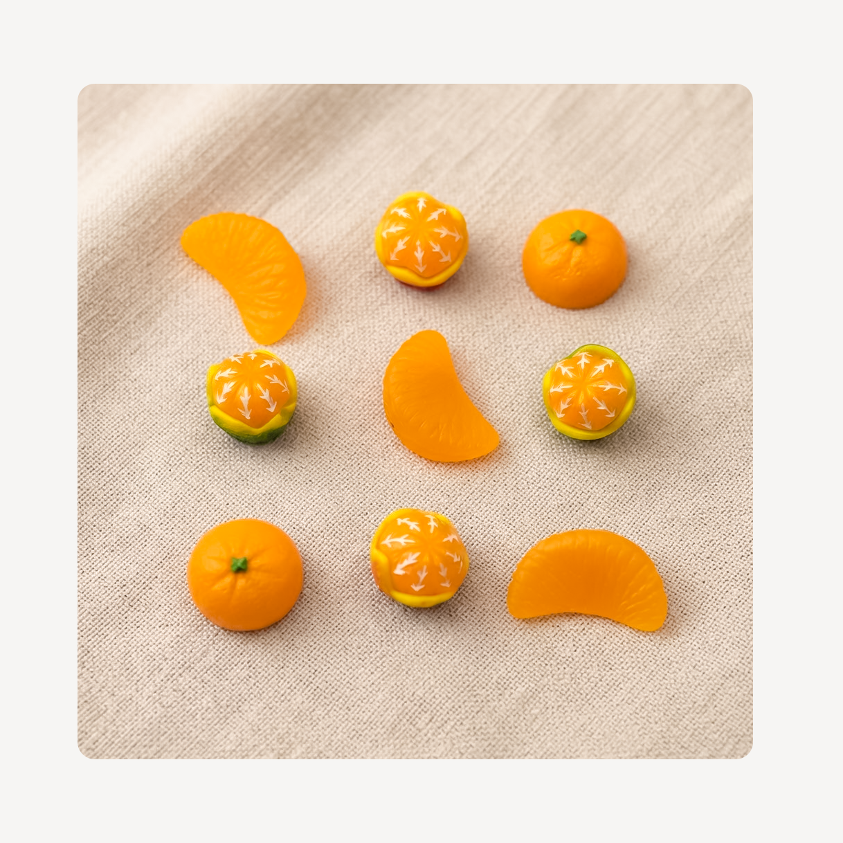 Nine miniature orange-themed clog charms arranged on a beige linen-textured surface. The set includes whole oranges, orange slices, and oranges with white starburst patterns resembling citrus pith or decorative detailing.