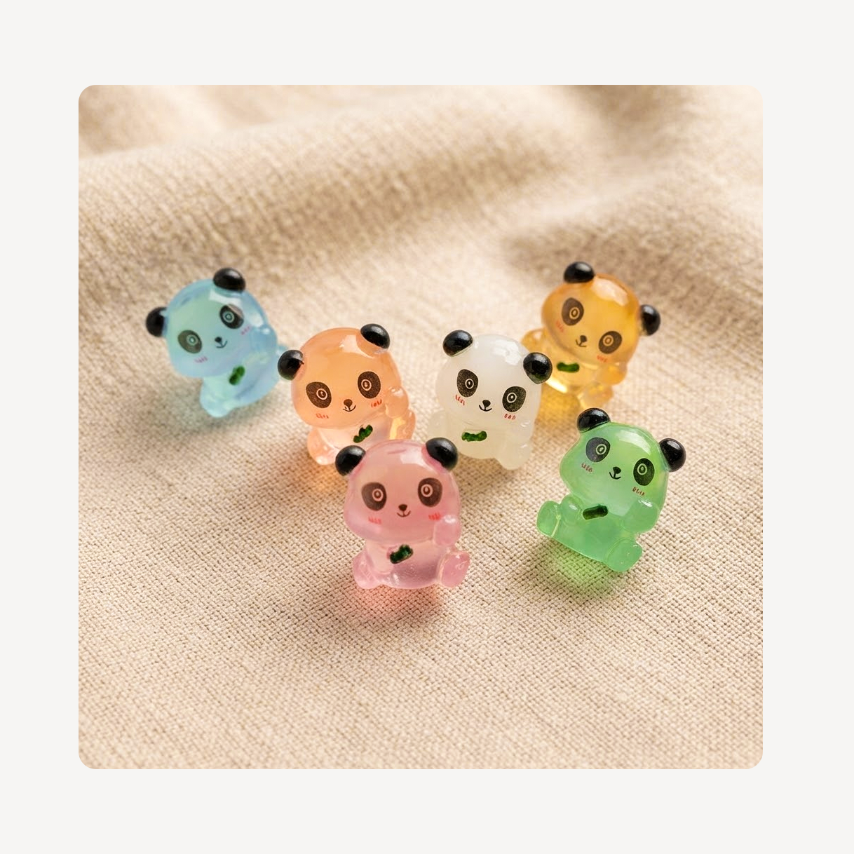 Six small translucent panda-shaped clog charms in pastel colors, including blue, peach, white, yellow, pink, and green, arranged on a beige fabric background.