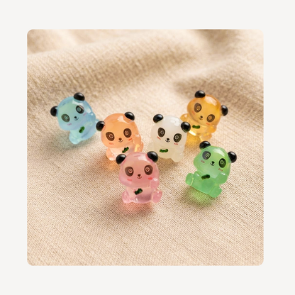 Six small translucent panda-shaped clog charms in pastel colors, including blue, peach, white, yellow, pink, and green, arranged on a beige fabric background.