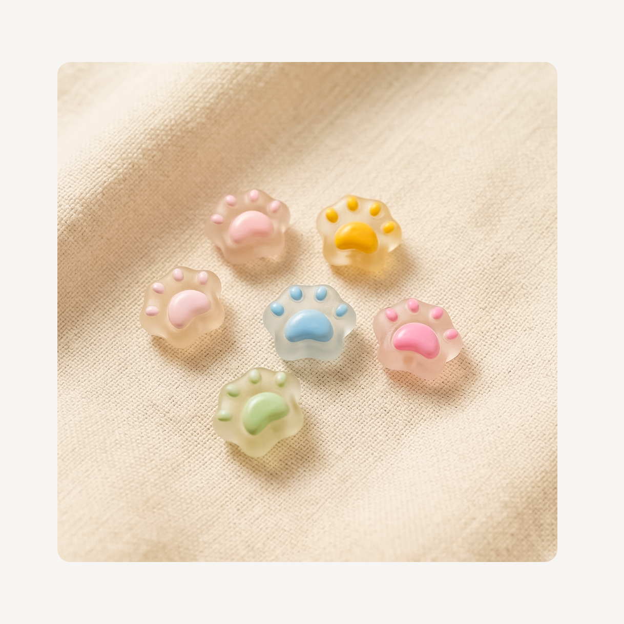Six small translucent paw-print clog charms in pastel colors, including pink, yellow, blue, green, and peach, arranged on a beige fabric background.