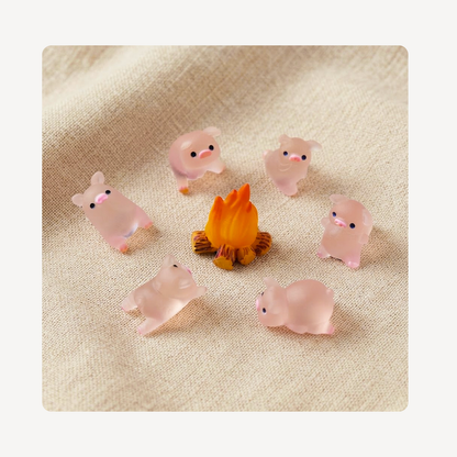 Six small translucent pink piggy clog charms arranged around a tiny orange campfire on a beige fabric background.