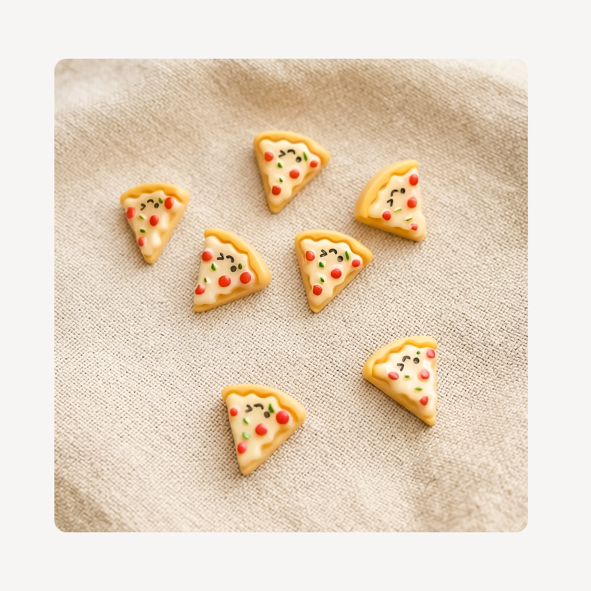 Six small triangular pizza slice-shaped clog charms with cute cartoon faces, arranged on a beige textured fabric background.