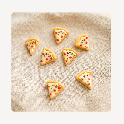 Six small triangular pizza slice-shaped clog charms with cute cartoon faces, arranged on a beige textured fabric background.