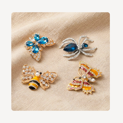 Four insect-themed rhinestone clog charms arranged on a beige textured fabric background: a blue flower, a blue spider, a yellow-and-black bumblebee, and a yellow-and-red butterfly.
