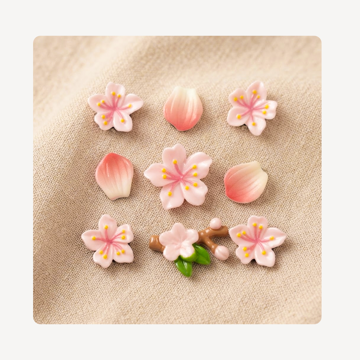 A set of nine cherry blossom-themed clog charms arranged on a textured beige fabric background. The set includes five pink and white cherry blossom flowers with yellow stamens, three pink petals, two small green leaves, and one branch detail.