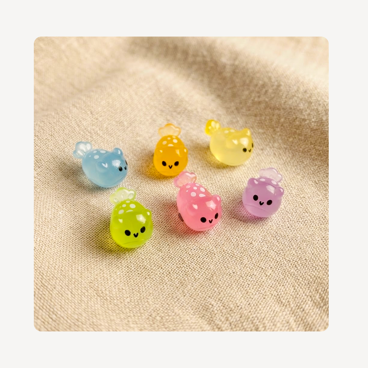 Six small translucent sea slug clog charms in pastel colors, including blue, yellow, green, pink, and purple, arranged on a beige textured fabric background.