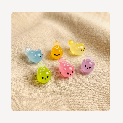 Six small translucent sea slug clog charms in pastel colors, including blue, yellow, green, pink, and purple, arranged on a beige textured fabric background.