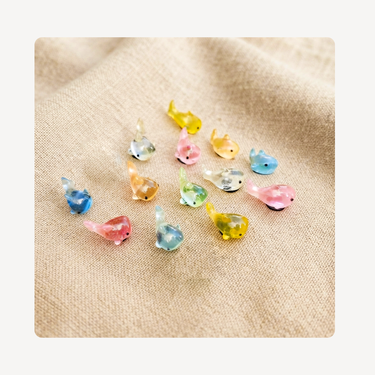A group of small translucent shark-shaped clog charms in pastel colors including blue, pink, yellow, green, and orange, arranged on a beige fabric background.