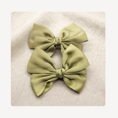 Two olive green satin sneaker bows arranged on a textured beige fabric background.