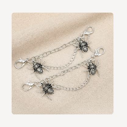 Two silver shoe chains with spider charms, displayed on a textured beige fabric background.