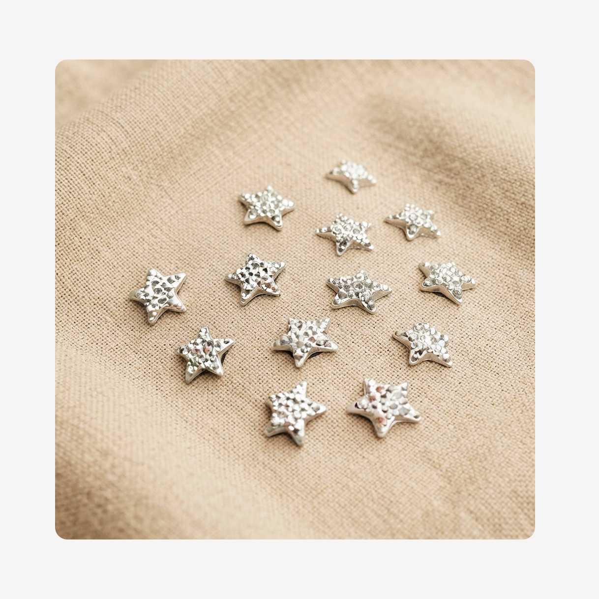 A group of small silver star-shaped clog charms with a textured surface, arranged on a beige linen fabric background.