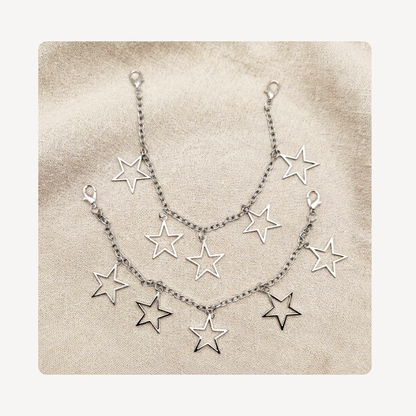 A silver-toned double-layered shoe chain featuring multiple dangling open star charms, displayed on a textured beige fabric background.