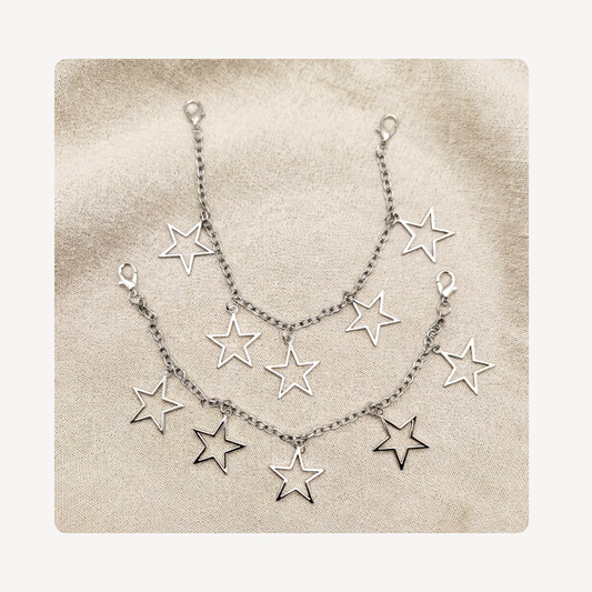 A silver-toned double-layered shoe chain featuring multiple dangling open star charms, displayed on a textured beige fabric background.