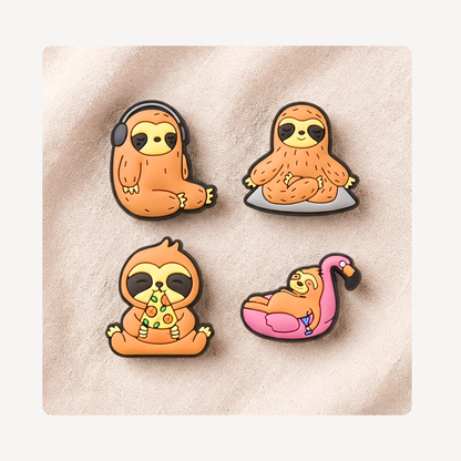 Four cartoon sloth-themed clog charms arranged on a light beige textured fabric background: one sloth wearing black headphones, one sloth sitting on a gray cushion, one sloth eating pizza, and one sloth resting on a pink flamingo float.