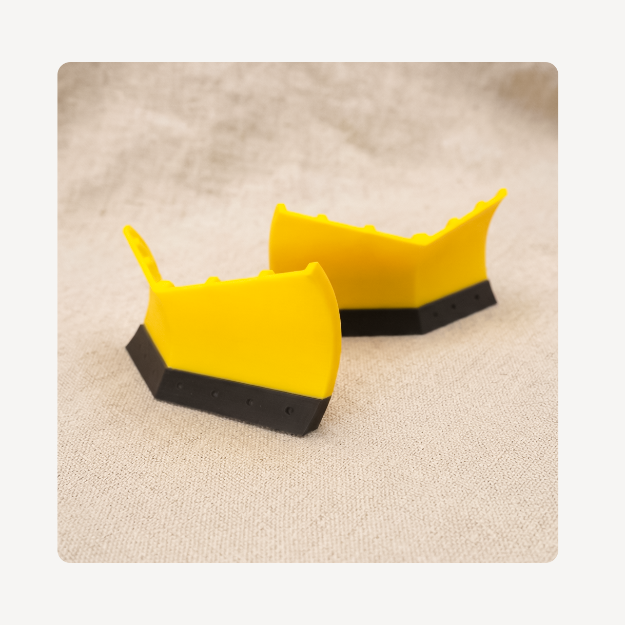 Two yellow and black snow plow clog charms displayed on a textured beige fabric background.